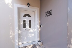 A white door with a decorative arch and two glass panels, a welcome sign, a mailbox, and a potted plant. - Effie's Escape Spacious House in Zola (Argostoli)