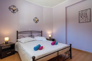 A neatly made bed with white linens, two bedside lamps, and a wall with a decorative metal piece and a framed picture. - Effie's Escape Spacious House in Zola (Argostoli)