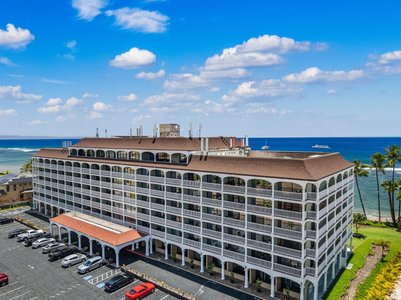 A multi-story hotel with a central courtyard, a parking lot, and a view of the ocean.