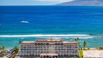 A multi-story hotel with a parking lot, located near a beach with ocean views.