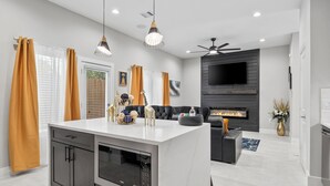A modern kitchen with a central island, built-in appliances, and a dining area with a sofa and fireplace. - Smart 3BR Home + Luxe Decor + Bluetooth Audio (Houston)