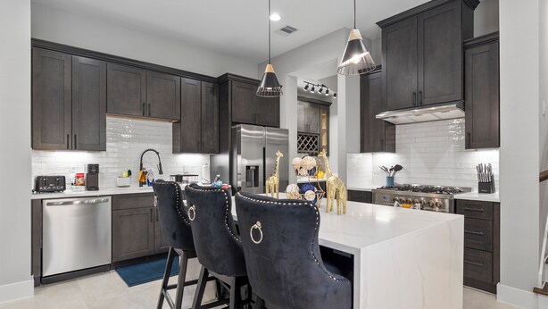 A modern kitchen with dark cabinetry, stainless steel appliances, and a central island with bar stools. - Smart 3BR Home + Luxe Decor + Bluetooth Audio (Houston)