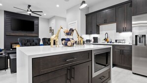 A modern kitchen with dark wood cabinets, a stainless steel refrigerator, and a white countertop. - Smart 3BR Home + Luxe Decor + Bluetooth Audio (Houston)