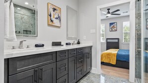 A modern bathroom with a large mirror, dark cabinets, and a shower area. - Smart 3BR Home + Luxe Decor + Bluetooth Audio (Houston)