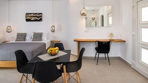 A modern bedroom with a bed, bedside table, and a small desk area with a chair. There is a fruit bowl on the desk and a mirror above it. - Alizea Villa (Santorini)