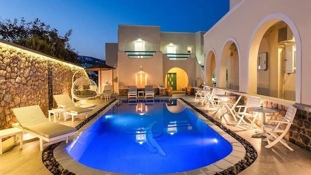 A swimming pool with lounge chairs and tables, surrounded by stone walls and arched doorways. - Alizea Villa (Santorini)