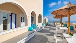 A rooftop terrace with white furniture, blue cushions, and thatched umbrellas. - Alizea Villa (Santorini)