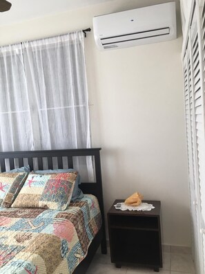 Ein Schlafzimmer mit einem Bett, einem Nachttisch, einer Klimaanlage und einem Fenster mit Jalousien.