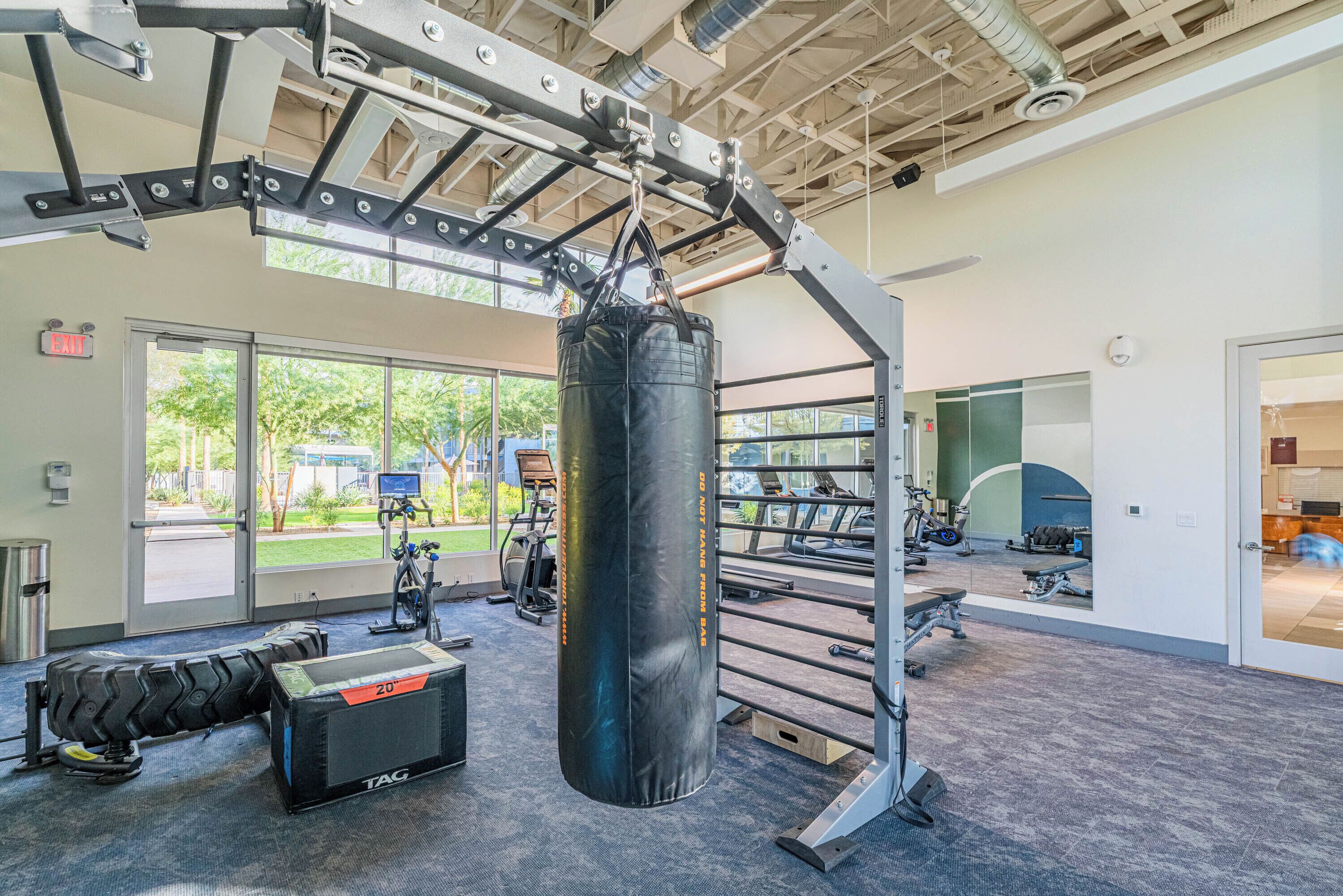 A gym with a punching bag, exercise equipment, and large windows offering views of the outdoors.