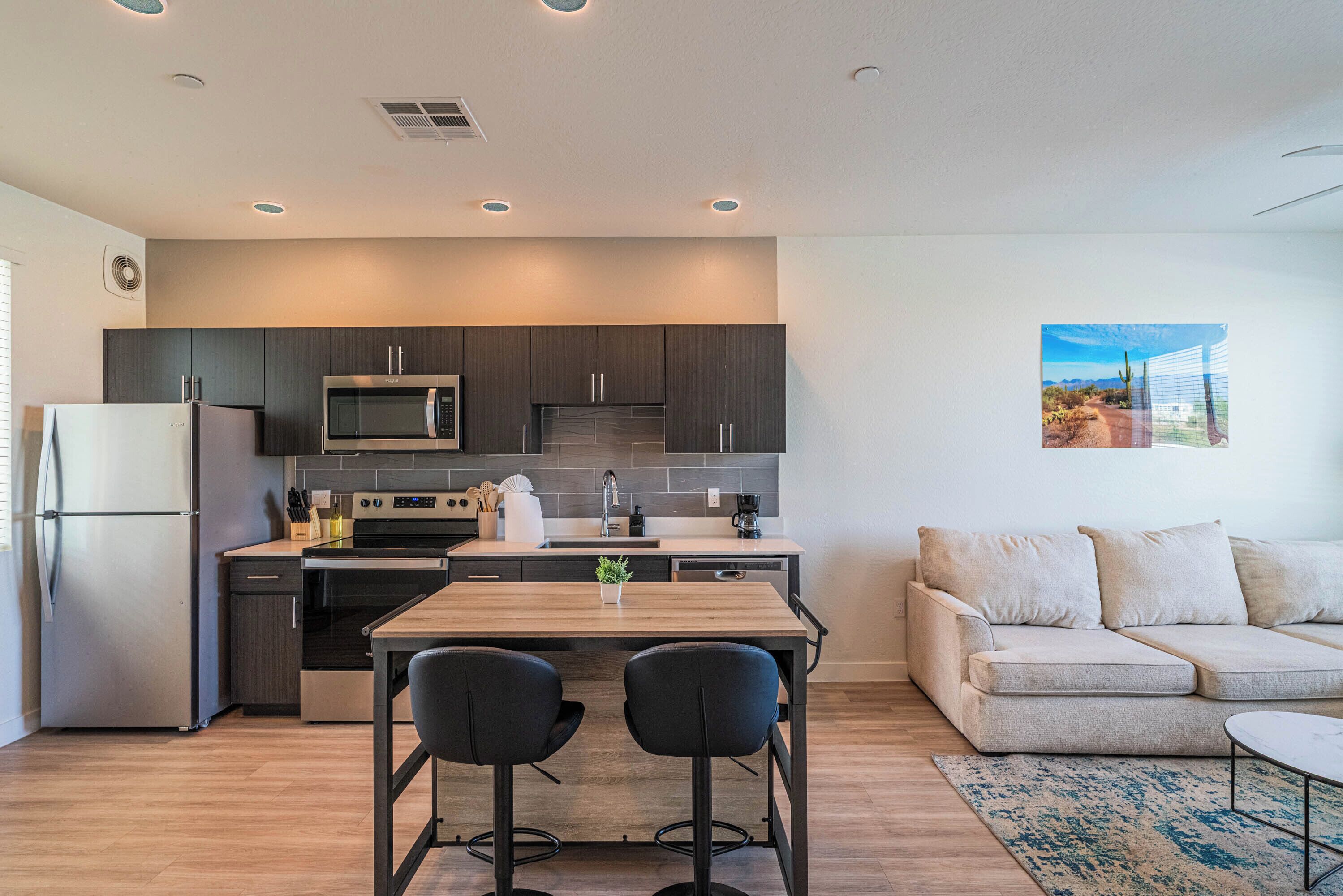A modern kitchen with dark cabinets, stainless steel appliances, and a wooden dining table with two chairs.