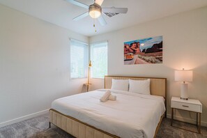 Ein Schlafzimmer mit Bett, Deckenventilator, Nachttisch, Lampe und einem Wandbild.