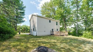 A two-story house with a fenced deck, surrounded by trees and a grassy yard. - •	Quiet 3BR Home Close to Biddeford Beaches (Biddeford)