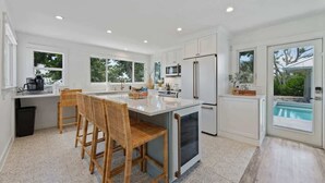 Una cucina moderna con mobili bianchi, una grande isola e vista su una piscina.