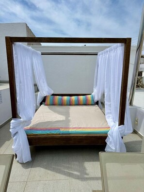 A bed with a wooden frame, white curtains, and colorful pillows on a balcony. - Mirinda Villa (Santorini)