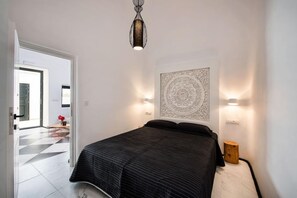 A bedroom with a bed, a wall-mounted light fixture, and a decorative wall piece. - Mirinda Villa (Santorini)