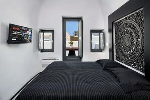 A bedroom with a large bed, a television mounted on the wall, and a decorative wall panel. - Mirinda Villa (Santorini)