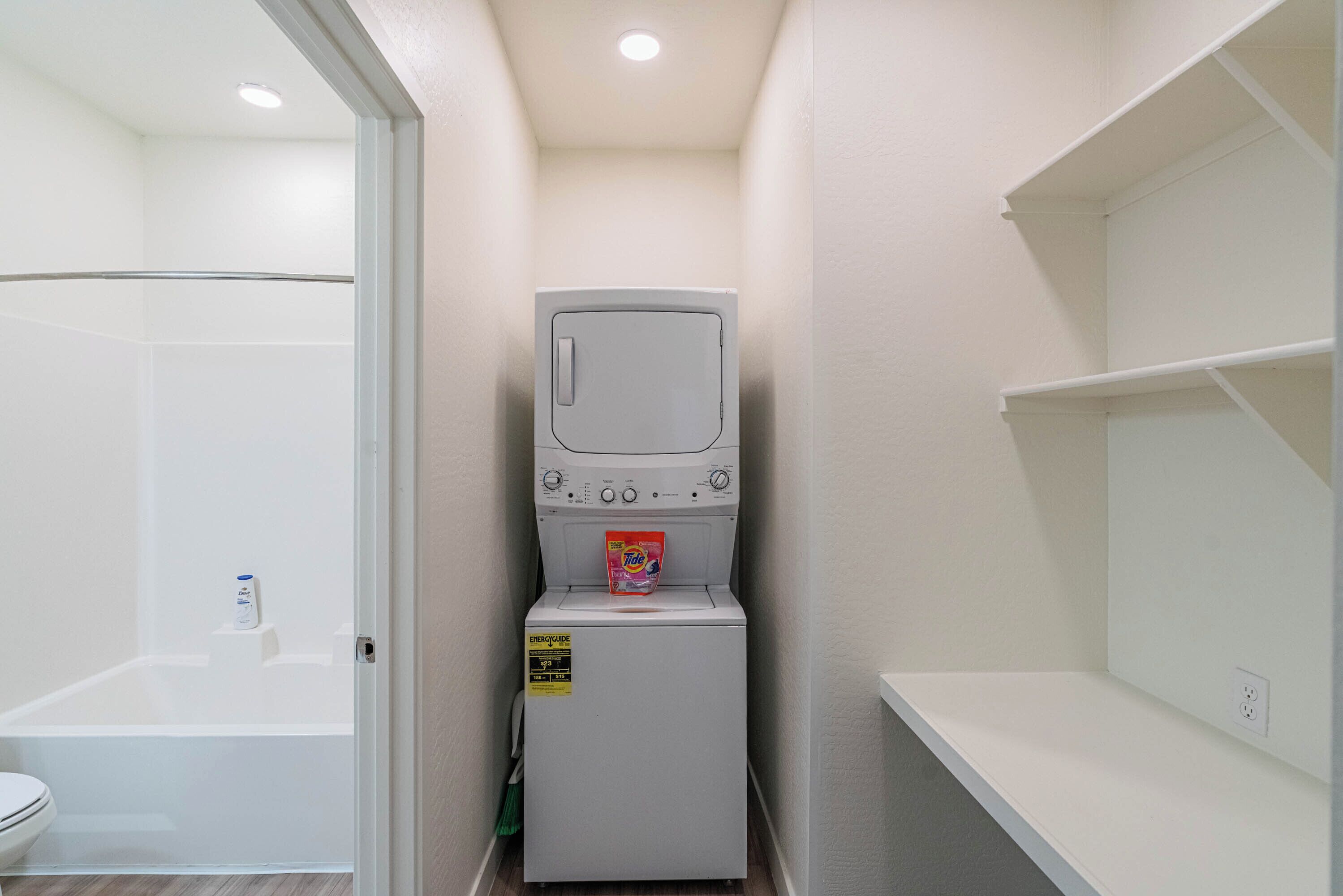 A compact laundry room with a washing machine, a small shelf, and a shower area.