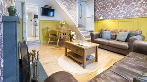 A living room with a brown leather sofa, wooden coffee table, and a yellow wall. - Hillside - Two bedroom Terrace, 1-mile from Silecroft Beach - Dog-friendly (Silecroft)