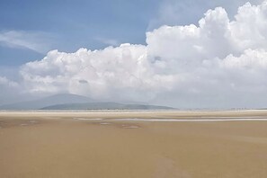 Una platja amb amplis arenals i una muntanya a la distància sota un cel amb núvols dispersos.