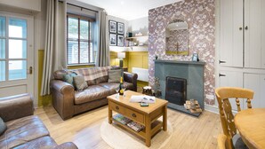 A cozy living room with a brown leather sofa, a wooden coffee table, and a fireplace. - Hillside - Two bedroom Terrace, 1-mile from Silecroft Beach - Dog-friendly (Silecroft)