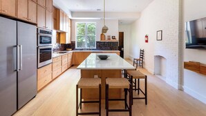 Une cuisine moderne avec des meubles en bois, des appareils en acier inoxydable, un îlot central doté de tabourets de bar et une cheminée.