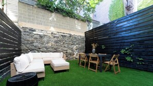 A backyard with a sectional sofa, a dining table with chairs, and a round black ottoman.