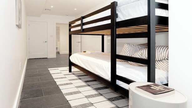 A bunk bed with a striped pillow, a white rug, and a small white table with a book.