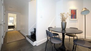 A modern living room with a round table and four chairs, a staircase, and a hallway leading to a bedroom.