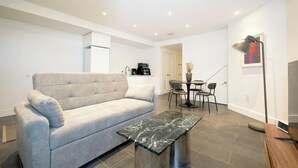 A modern living room with a grey sofa, a marble coffee table, a dining area with a small table and chairs, and a painting on the wall.