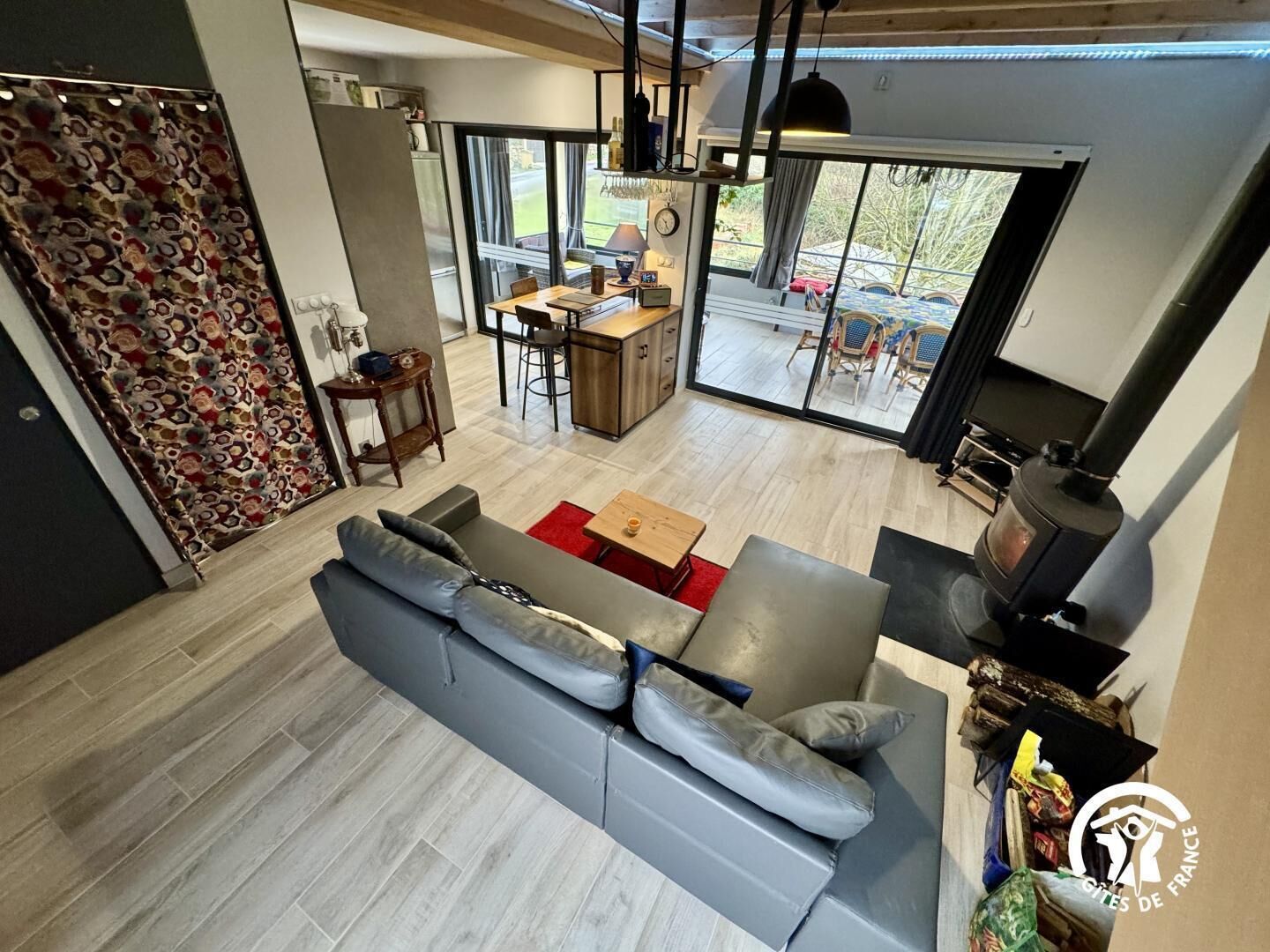 A modern living room with a grey sofa, a wooden dining table, and a kitchen area with a stove.