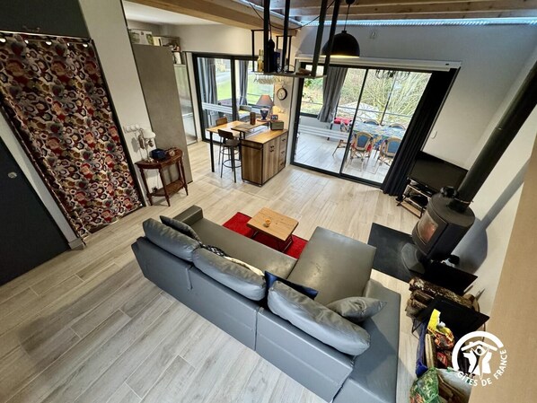 A modern living room with a grey sofa, a wooden dining table, and a kitchen area with a stove. - Sissou - BUGARACH - Gîte (BUGARACH)