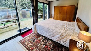 Un dormitorio con una cama grande, un armario de madera, un tapete de diseño rojo y negro, y vistas al jardín trasero a través de una puerta corrediza de vidrio.