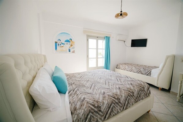 A bedroom with a large bed, a smaller bed, a TV, and a window with curtains.