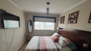 Ein Schlafzimmer mit einem Bett, einem Nachttisch, einem Spiegel und einem Fenster mit Jalousien.