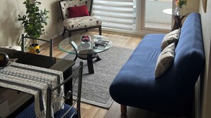 Ein Wohnzimmer mit einer Couch, einem Sessel, einem Glastisch, einem an der Wand montierten Fernseher und einem Deckenventilator.