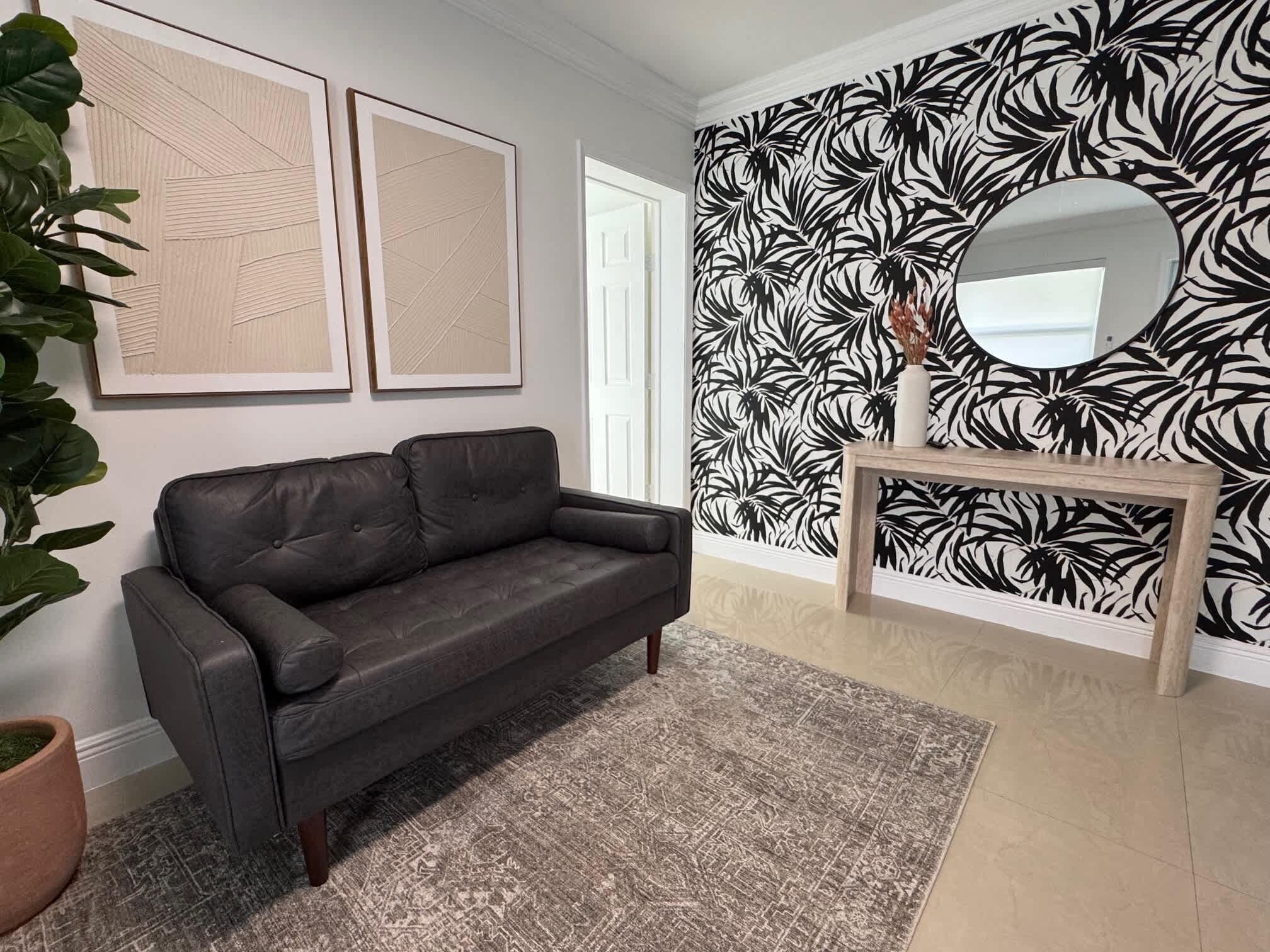 A modern living room with a dark leather sofa, a patterned rug, and a wall with a black and white leaf design.