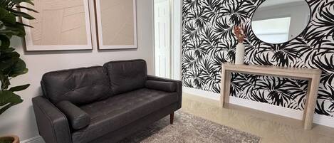 A modern living room with a dark leather sofa, a patterned rug, and a wall with a black and white leaf design.