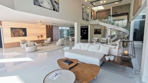 Ein großzügiger Wohnbereich im modernen Stil mit einem großen weißen Sofa, einem Couchtisch und einem Essbereich mit einer Wendeltreppe.