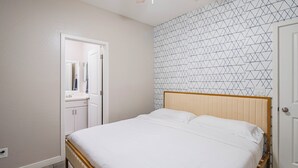 A bedroom with a bed, a wardrobe, a mirror, and a geometric-patterned wall. - The One 112 (Glendale)