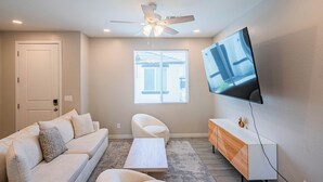 A modern living room with a sofa, coffee table, TV, and a ceiling fan. - The One 112 (Glendale)