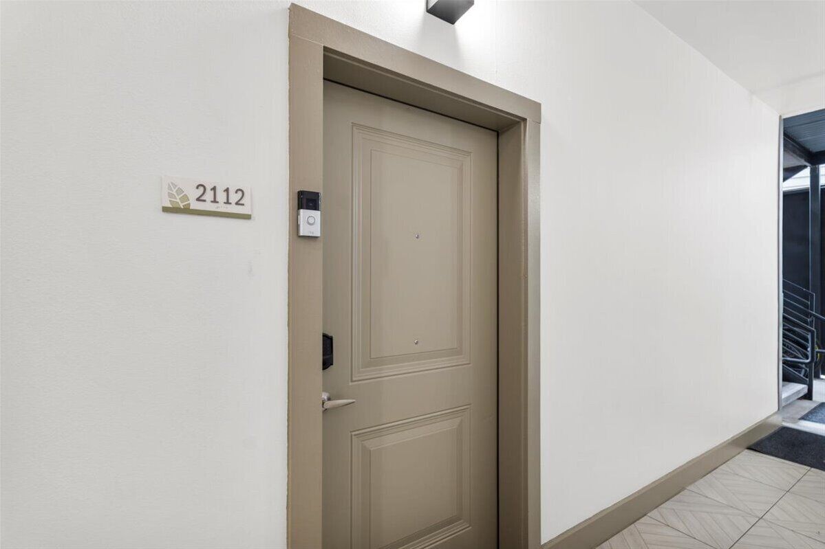 A beige door with a number plate '2112' and a doorbell on a white wall.