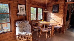 Interior de una cabaña de madera con una mesa de comedor, sillas, un sillón mullido y una lámpara colgante.