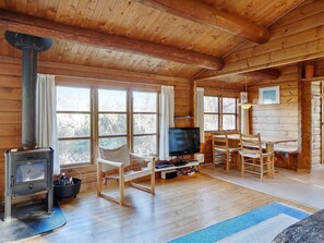 A log cabin interior with a wood stove, a television, and a dining area. - Nature oasis with private lake near beach (Fårevejle)