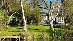 Una cabaña junto al lago con un muelle, rodeada de abundante vegetación y árboles.