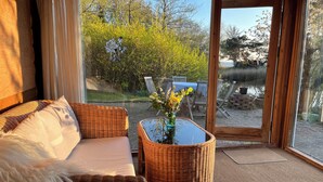 Una habitación con un sofá de mimbre, una mesa de centro de vidrio con un florero, y vistas a un espacio exterior con una mesa y sillas.
