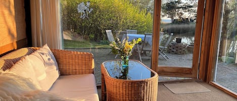 A room with a wicker sofa, a glass coffee table with a vase, and a view of an outdoor area with a table and chairs.