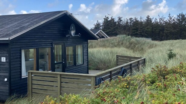 A cabin with a deck, large windows, and a satellite dish. - Welcome to this house in the dunes. (Løkken)