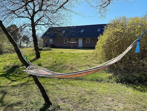 A hammock tied between trees in a grassy area with a house in the background.