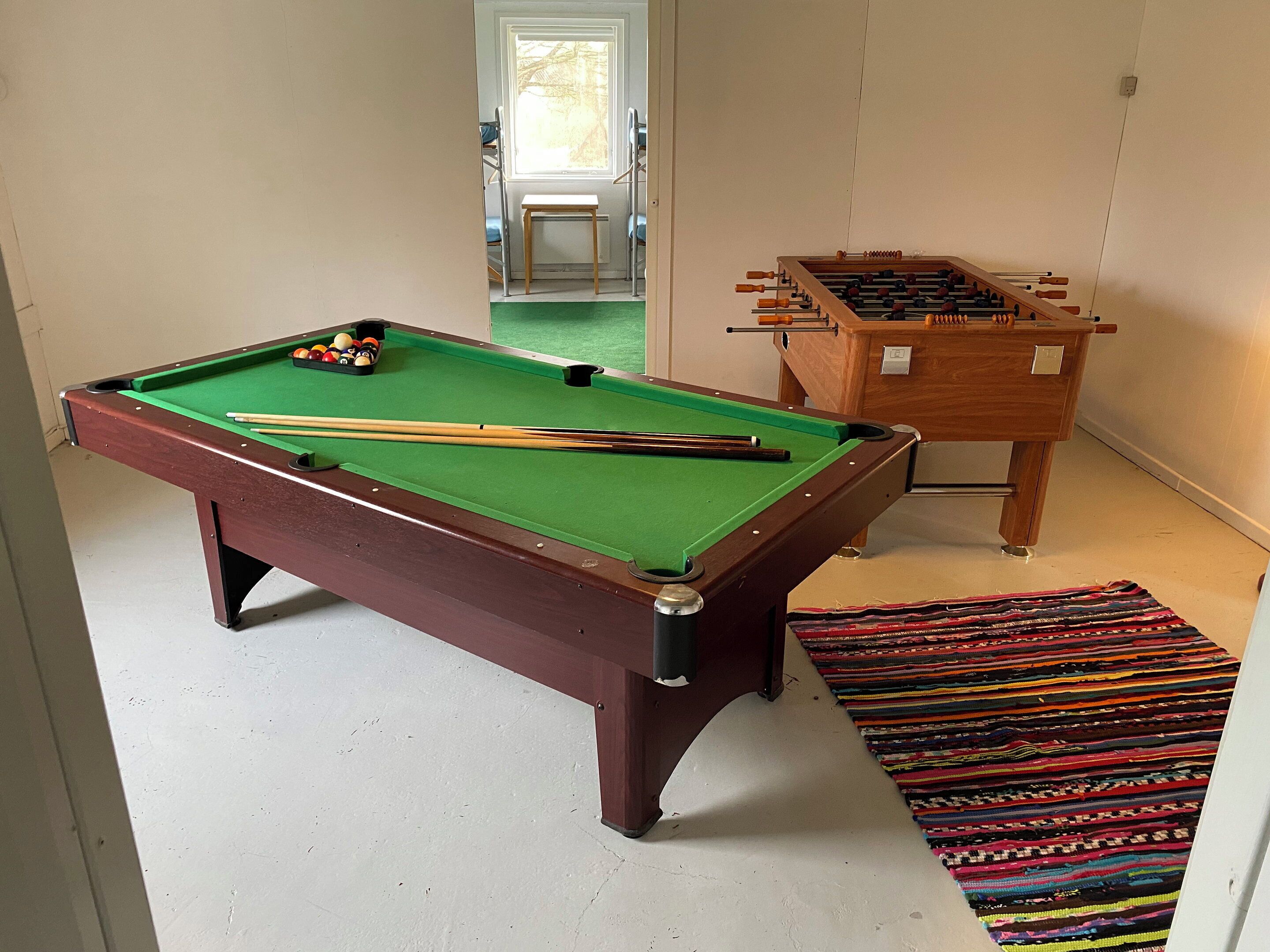 A pool table with balls and cues, a foosball table, and a colorful rug.