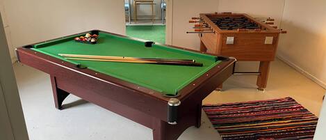 A pool table with balls and cues, a foosball table, and a colorful rug.
